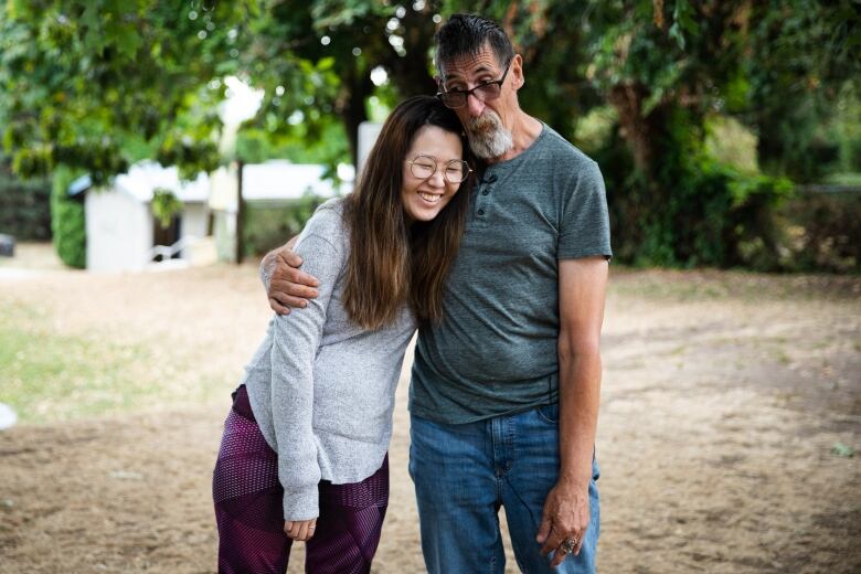 A younger woman wearing glasses and purple tights laughs as she leans in for a hug with an older bearded man.