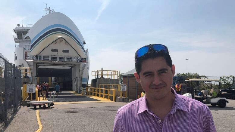 A man stands in front of a ferry boat. 