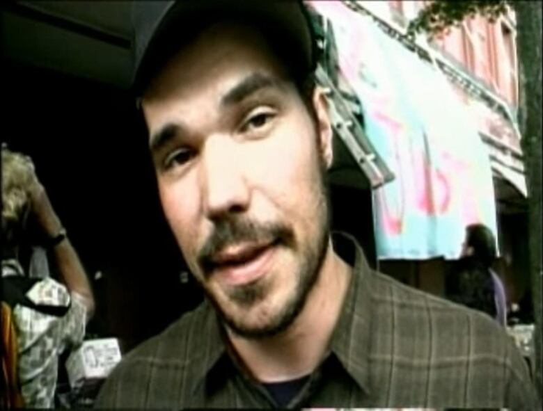 A young man looks quizzically at the camera in front of banners.