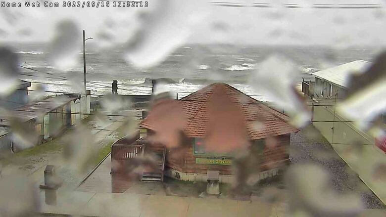 A rain-spattered view of a circular building on the coast of a stormy ocean. 