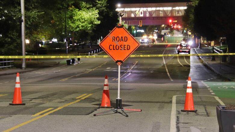 A tall 'ROAD CLOSED' sign in front of crime tape on a large street.