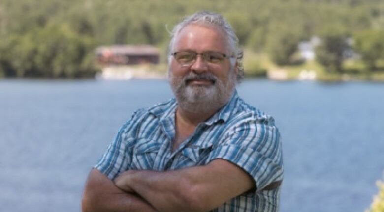 Raymond Blanger stands with his arms folded in front of a body of water.