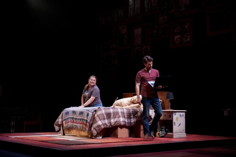 Salt Baby (Chanin Lee) sits on a bed decorated with a First Nations blanket, asking her boyfriend Phillip (Aris Athanasopoulos) to help her meditate. He is holding a laptop with the online meditation method on screen while facing away from her.