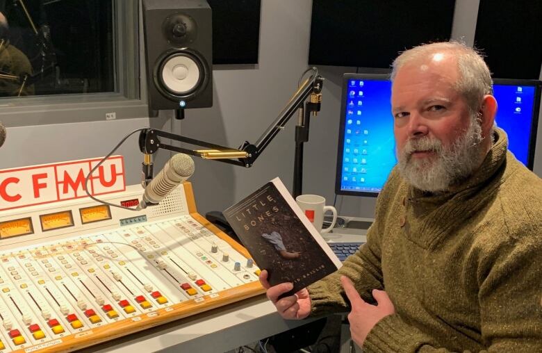 A man sitting in front of a soundboard in a radio studio.