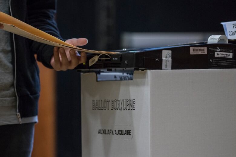 A person inserts a folder through a ballot box.