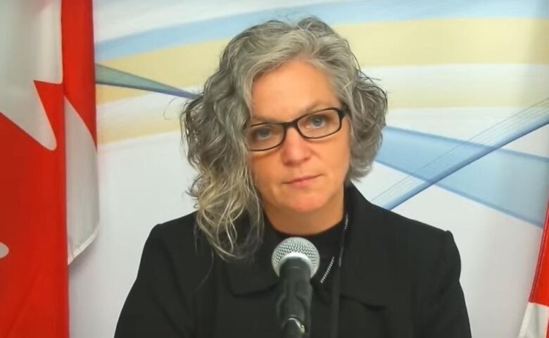 Woman in a black jacket sits in front of a microphone. 