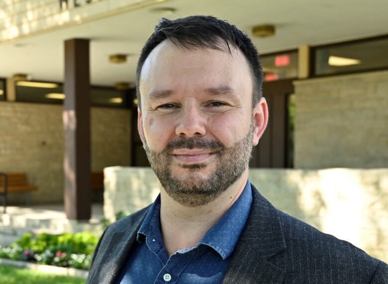 A man smiles in front of a library.