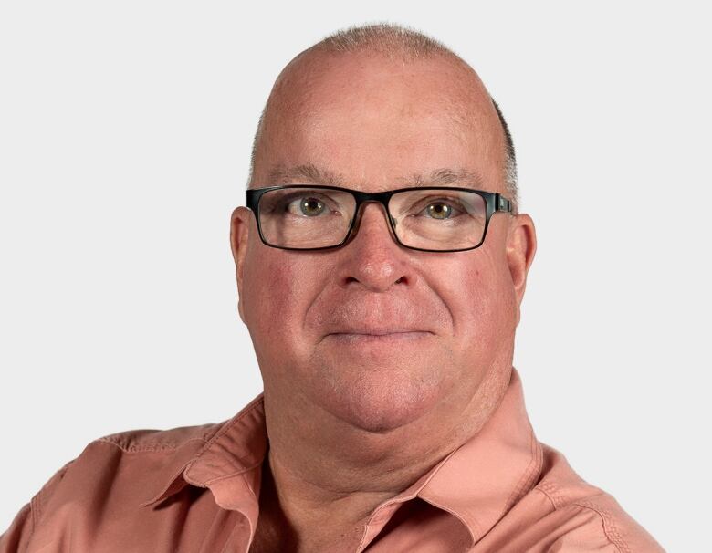 A bald man with glasses crosses his arms for the camera.