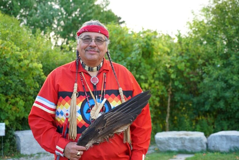 An indigenous elder holding an eagle feather stands at the centre of a ceremonial fire ground.