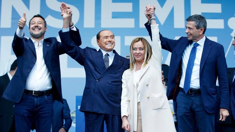 Three men and a woman raise their hands in triumph. 