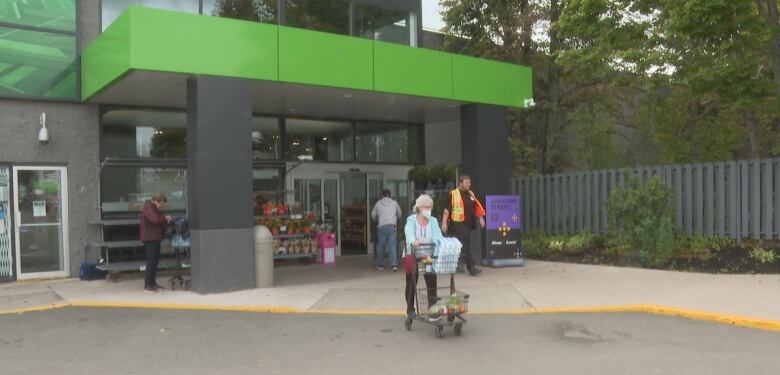 A woman pushes a shopping cart into a parking lot. 