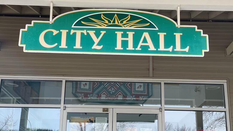 A door with a green sign hanging over it reading 'City Hall'.