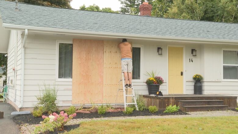 Man hammers nails into boards over window of a house.