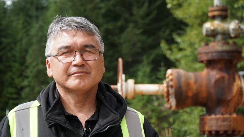 An older man stands in front of a forest.