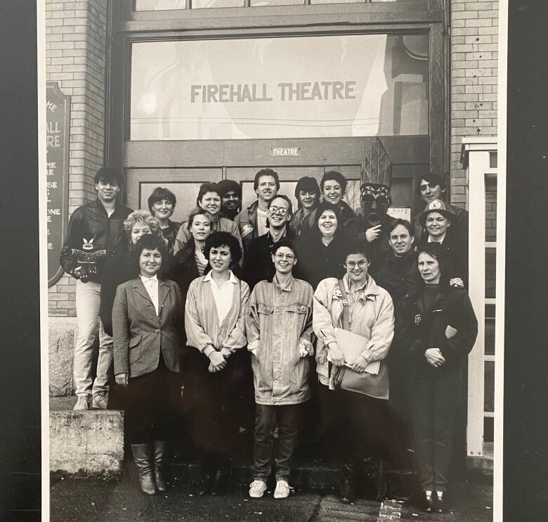 A black-and-white picture of a number of people gathered outside a building with a sign that reads 'Firehall Theatre'.