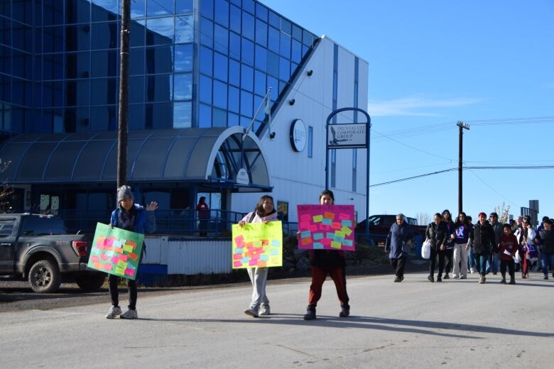 Three young people carrying posters lead a group walking down a street.