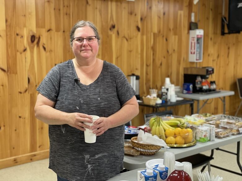 A woman stands next to a table full of fruits and pastries.