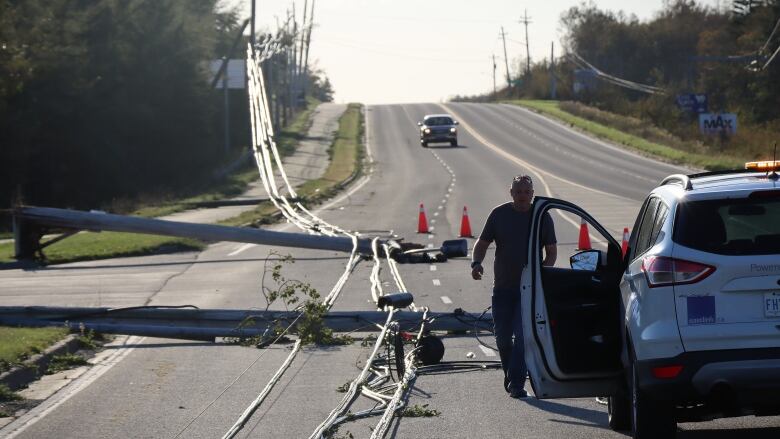 An Eastlink cable employee walks downed telecommunication lines at the entrance to J.A. Douglas McCurdy Sydney Airport. A truck is driving towards him. 