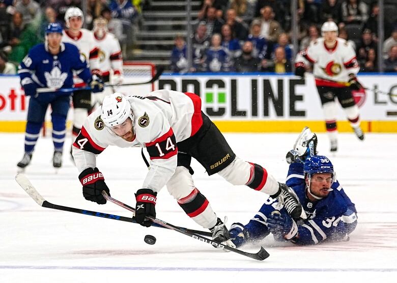 Two hockey players battle for the puck in the middle of the ice. One has fallen and the other looks like he's about to fall.