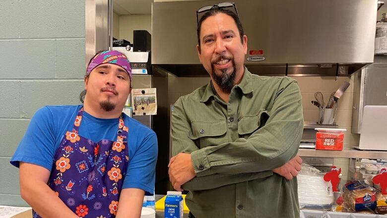 Two Indigenous men pose in a kitchen 