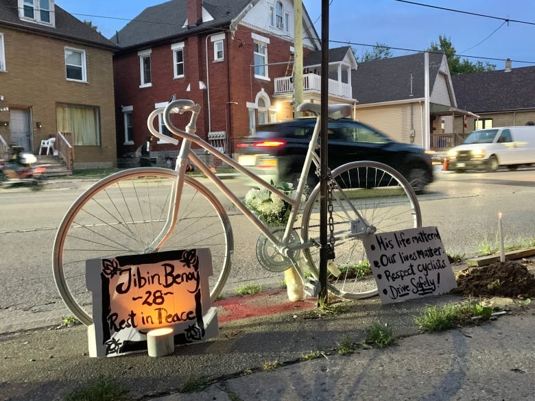 A white bike on the side of the road is surrounded by candles and signs saying 