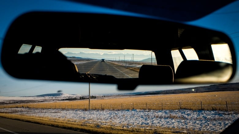 A car reflected in a rear view mirror drives through a field. 