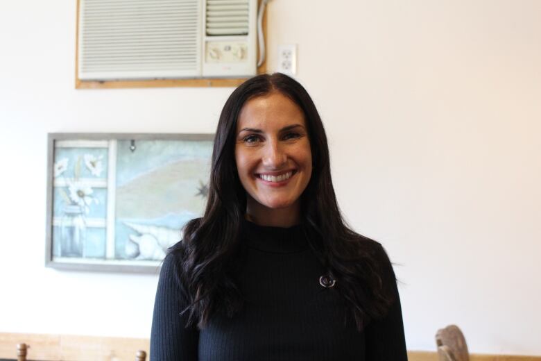 A woman with dark hair smiles in front of a white wall. 