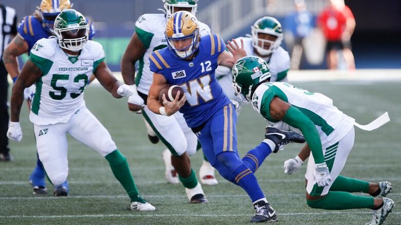 Four Saskatchewan Roughriders, in white, attempt to tackle a Winnipeg Blue Bomber, in blue.