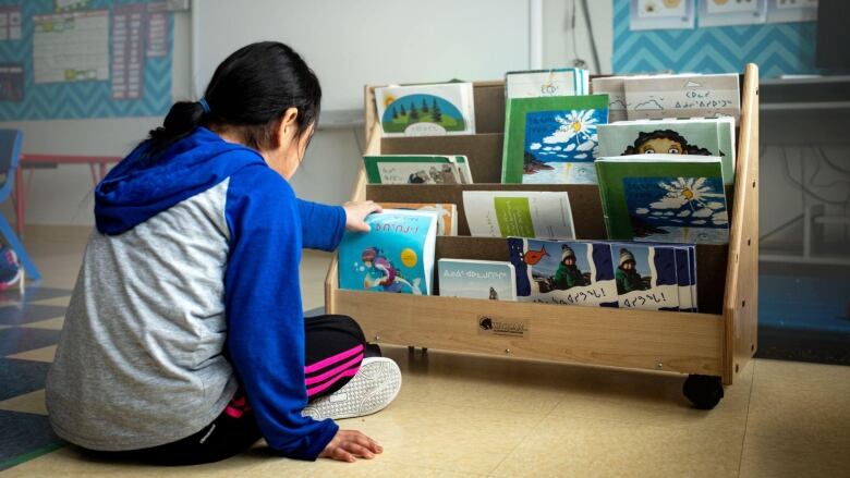 A child sitting in front of a bookshelf and picking up a book.