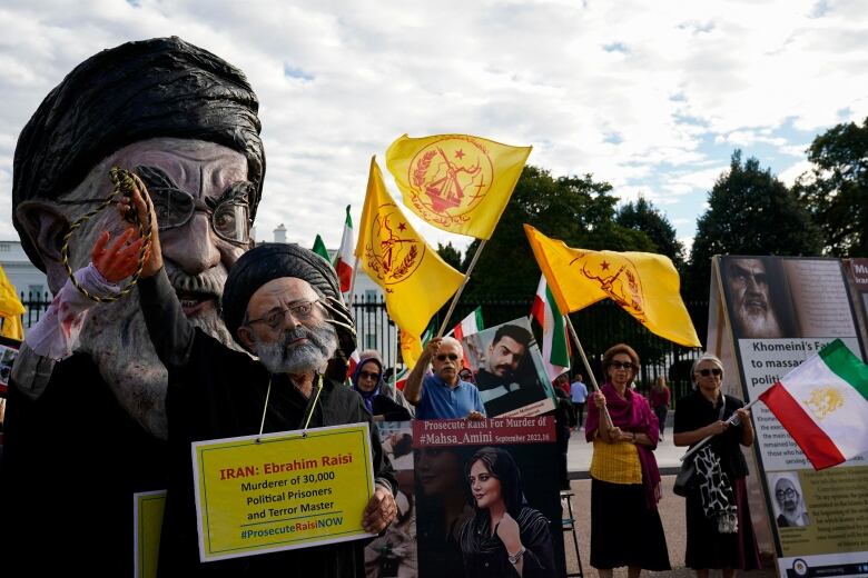 A group of people, protesting, some holding yellow flags with red writing on them.