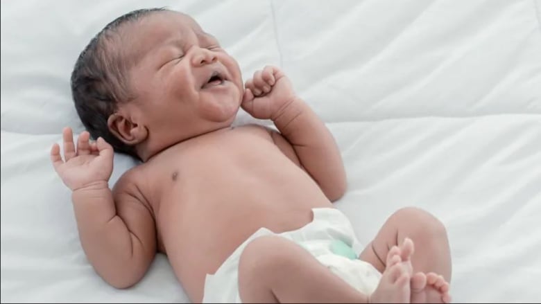 A baby, in a diaper, is lying down with eyes closed