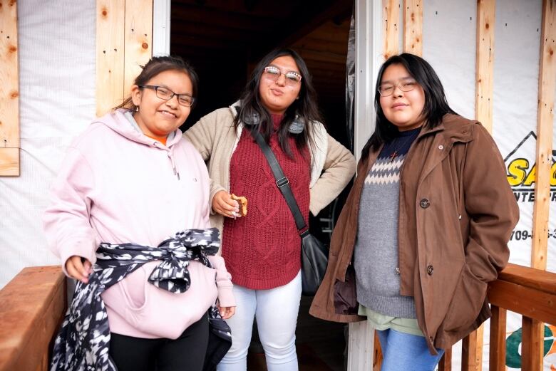 Three teenagers smile while standing at the entrance way to a cabin. 