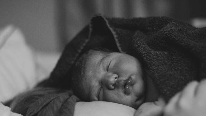 A black and white image of a sleeping newborn baby.