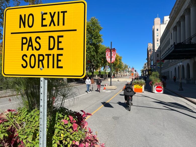 A woman wearing an orange shirt bikes past a big sign that says 