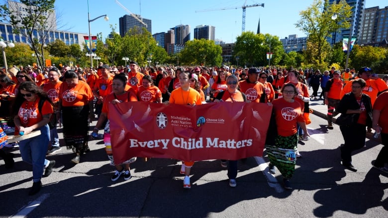 A group of people wearing orange shirts cary a red banner that reads 