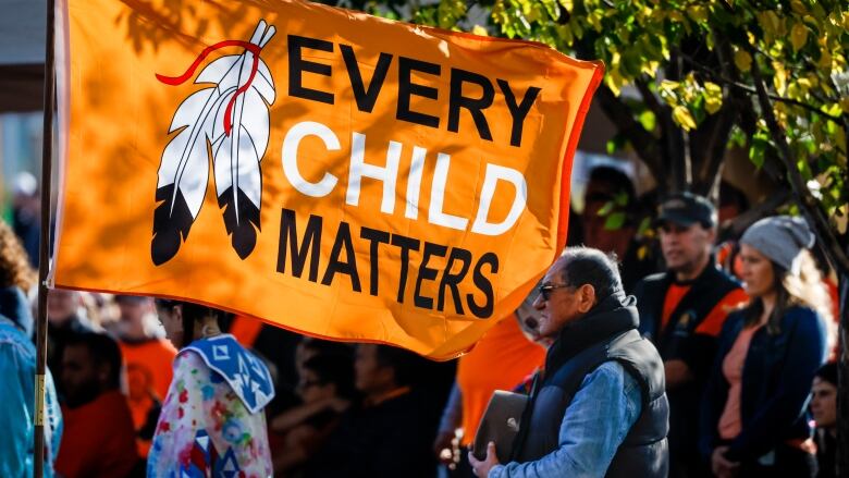 A crowd walks and carries an orange flag that says Every Child Matters 