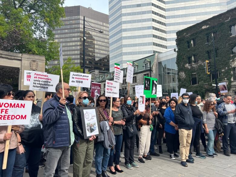 A large group of protesters, much of them Persian, crowd a university campus. 