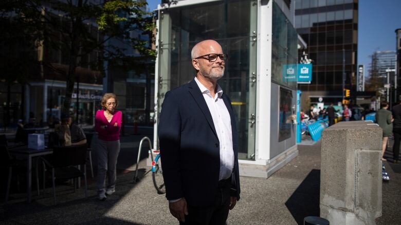 A white, middle-aged man in a suit stands on a sidewalk in downtown Vancouver.