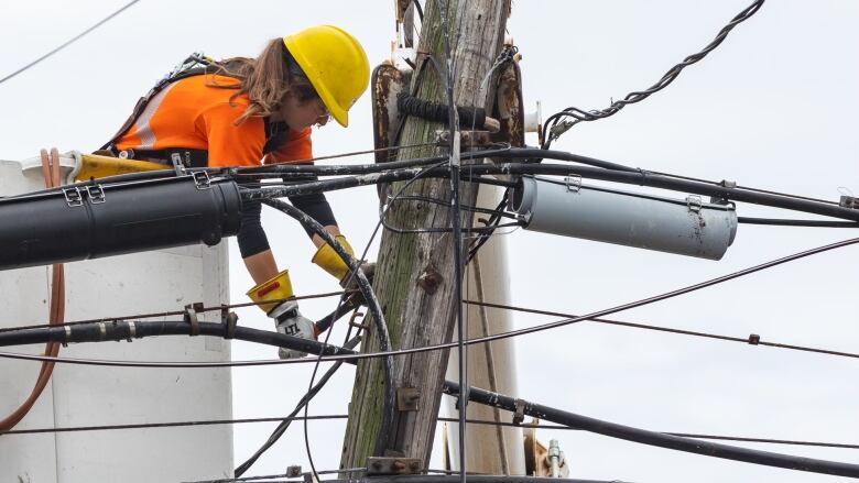 A worker in a yellow hard hat uses a tool on a power line.