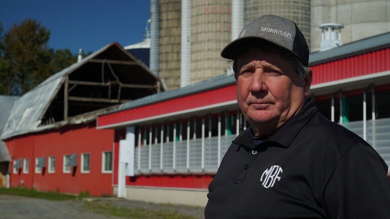 Denis Morris stands in front of his damaged barn, which is missing part of its roof.  