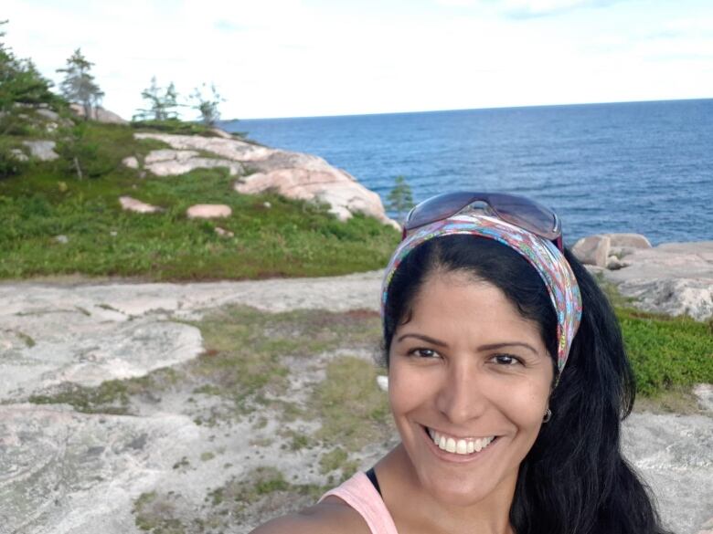 A woman smiles in front of a lake and trees. 