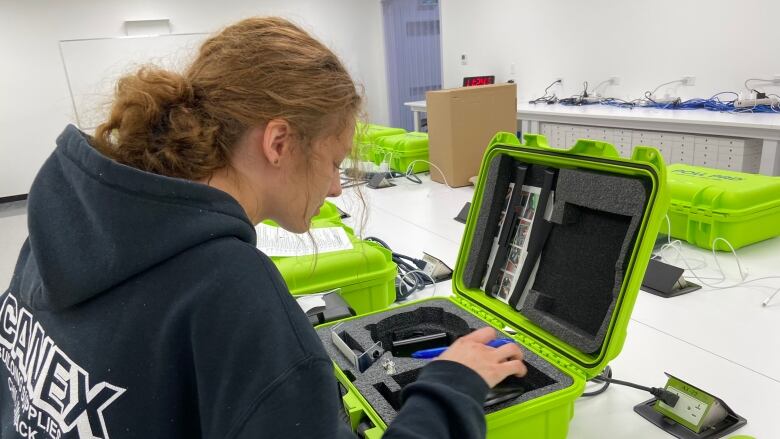 A woman in a hoodie looks into a bright green box that contains a voter check-in and verification tablet.