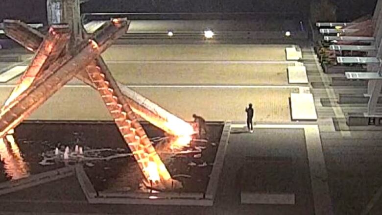 Two people are seen in the distance near a giant Olympic torch.