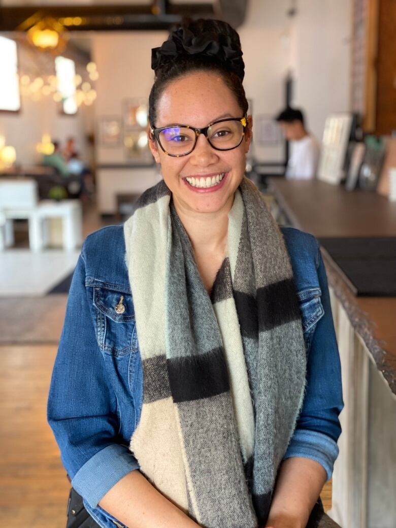 A woman smiles widely as she sits comfortably in a coffee shop. 