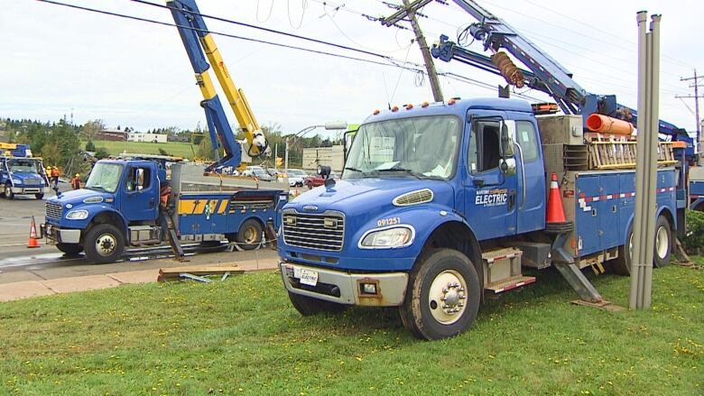 Three blue Maritime Electric trucks parked on the road. 