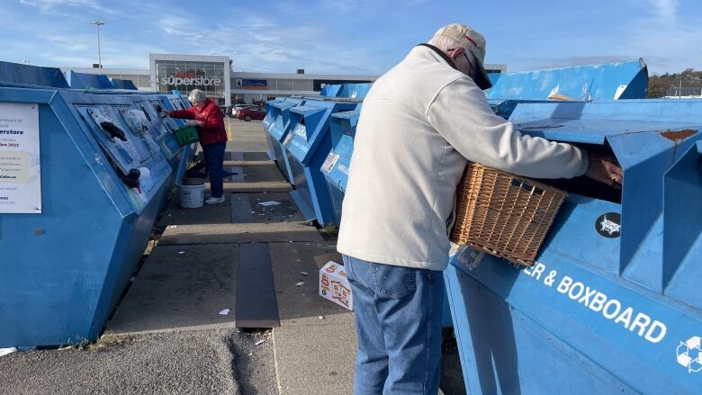 A man puts recycling into a blue bin labeled 