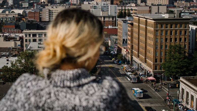 A woman with blonde hair is seen in silhouette, looking over a cityscape.