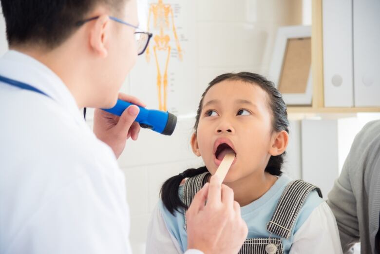 A young girl opens her mouth for a doctor doing oral examination.