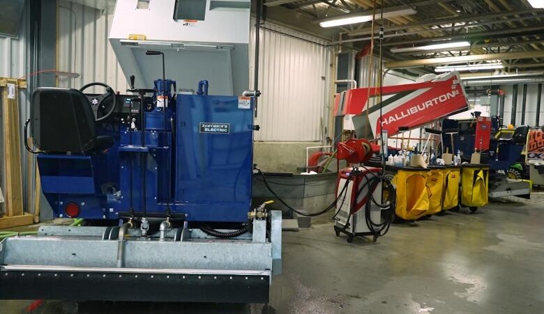 Two ice resurfacers in an arena garage. One is being recharged because it is electric. 