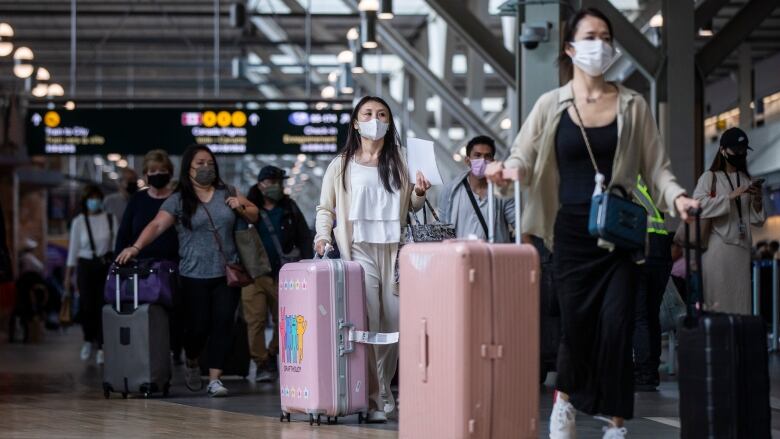 A group of masked people cart along suitcases in an airport.